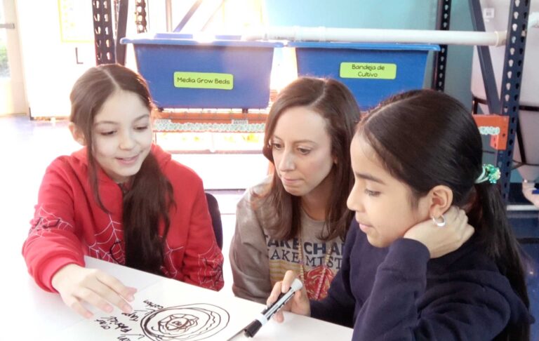 two young female students discuss their blueprint design with their teacher